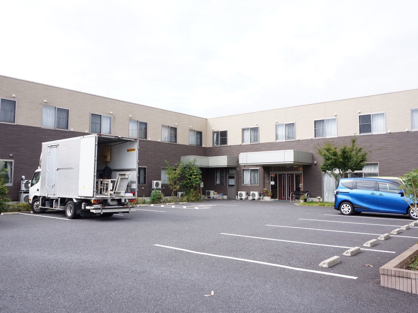 建物は二階建てで、ブラウンとベージュのツートンカラーである。建物の前には駐車スペースが広がっている。大型車両でも駐車できる。