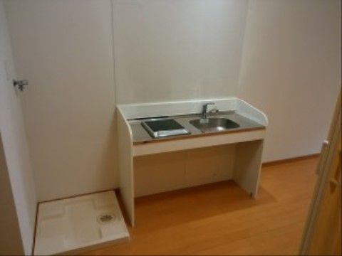 ミニキッチンにはIHタイプのコンロが一口ある。壁には飛び散り防止の透明なガードが付いている。隣には洗濯機が置けるスペースがある。
