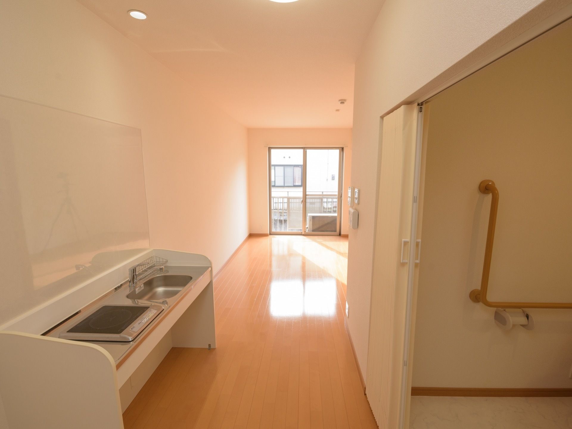 大きく扉が開くトイレの前に、キッチンが設置されている。正面には大きな窓があり、日当たりがいい。床には凹凸がない。