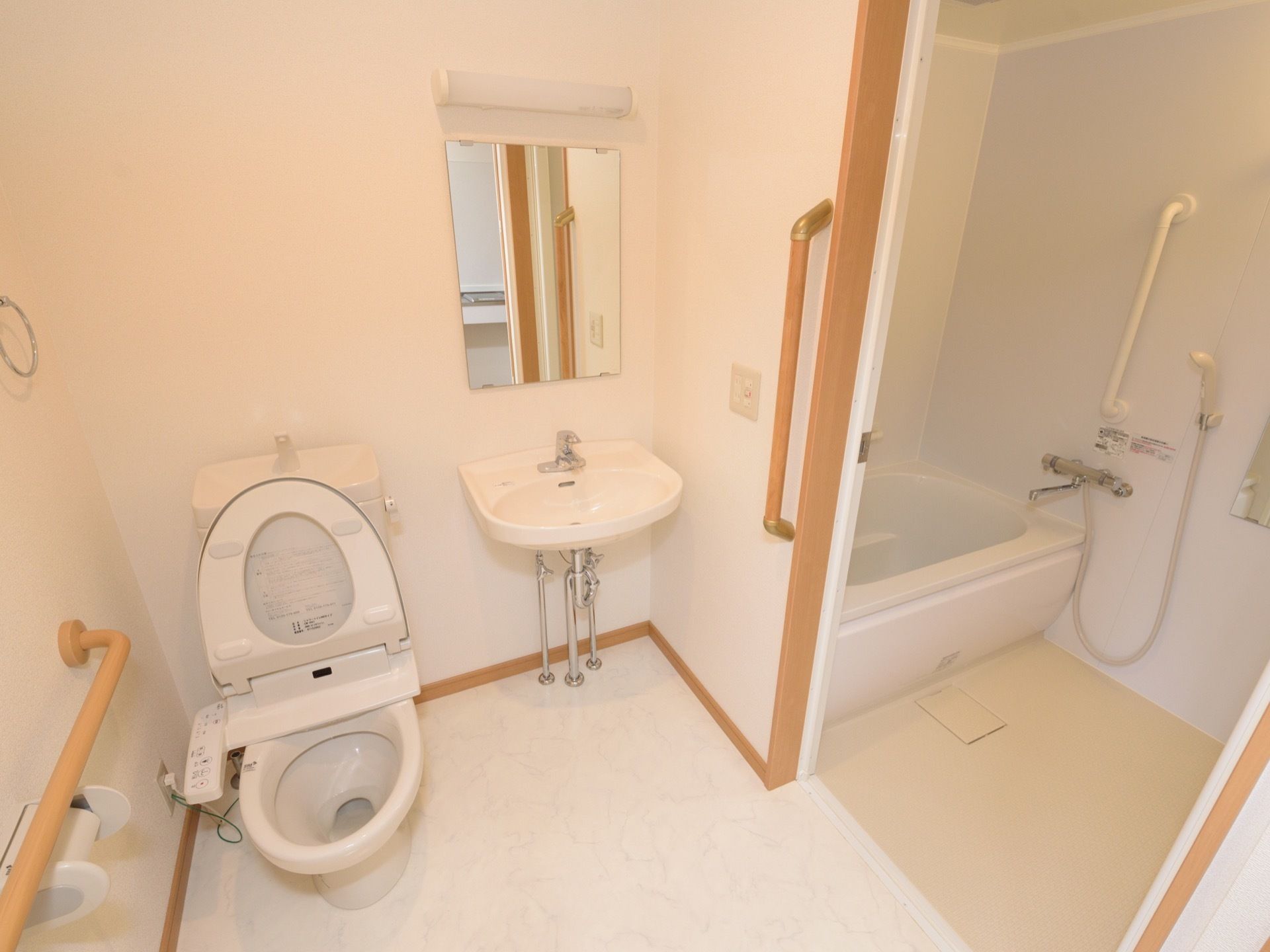 手前にトイレと洗面台、奥に浴室がある。トイレ内や浴室内、またその間の壁に手すりが設置されている。洗面台前には鏡とライトが付いている。