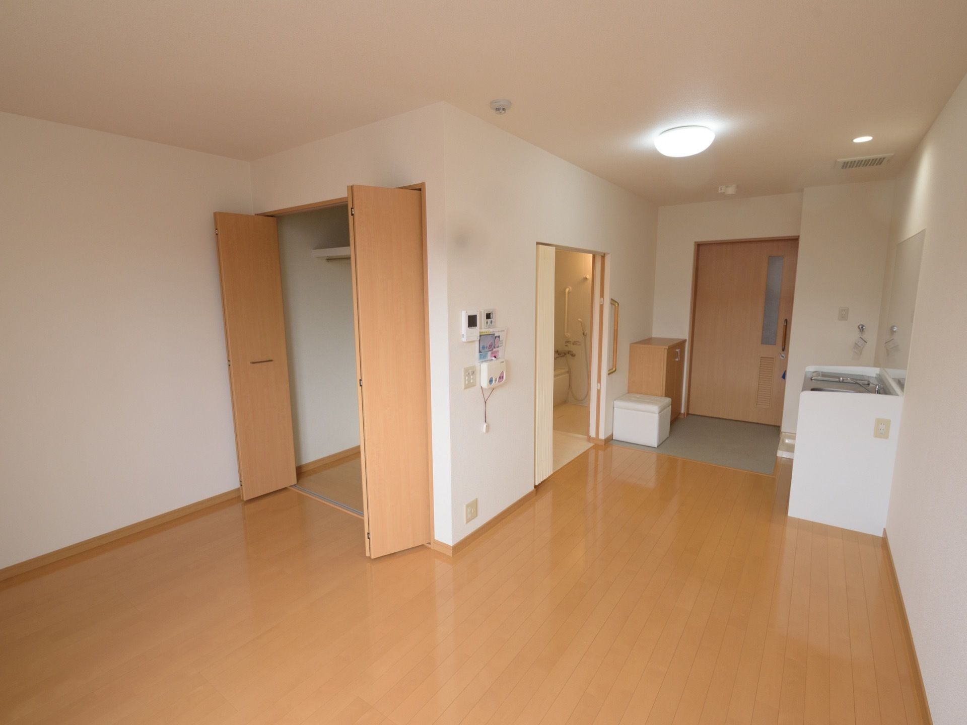 フローリングの床の居室である。入り口はスライドドアで、キッチンや収納、浴室などが備わっている。玄関にあたる部分に、靴箱が置かれている。