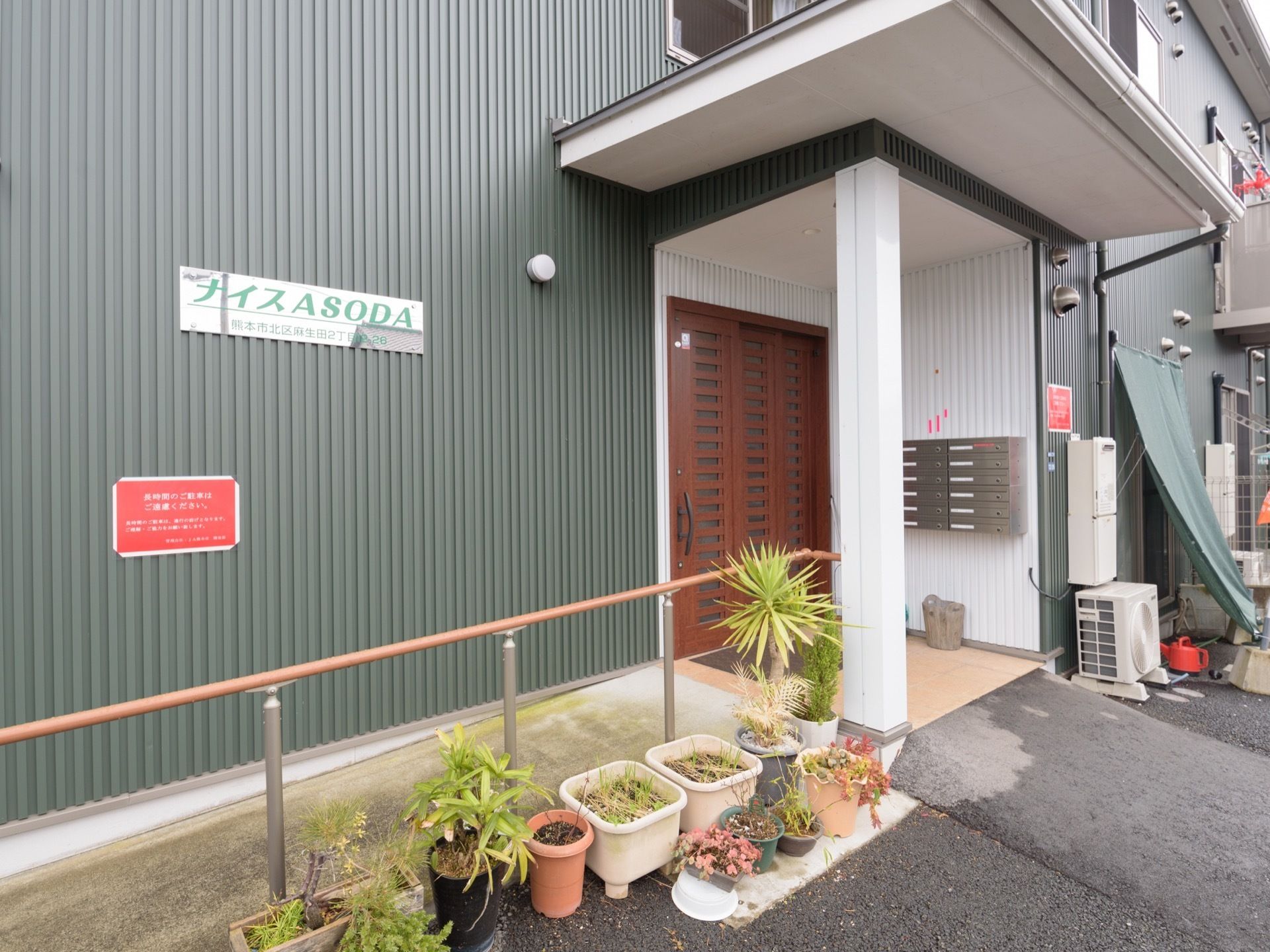 玄関の入り口横の外壁に、施設名の書かれたパネルが設置されている。玄関ポーチに向かって少し傾斜があるが、壁に沿ってスロープと手すりがある。
