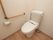 清潔感のある水洗トイレの横の壁には手すりがＬ字型に設置されている。周りに障害物が無く、広々としている。