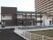 緑色の屋根が目を引く２階建ての建物。壁の色は焦げ茶がメインになっている。すぐ横には大きな団地がある。
