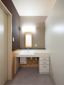 通路の突き当りに幅いっぱいに設置された角型で白い洗面台があり、腰の位置には引き出しが３つあり正面には細長い鏡がついている。