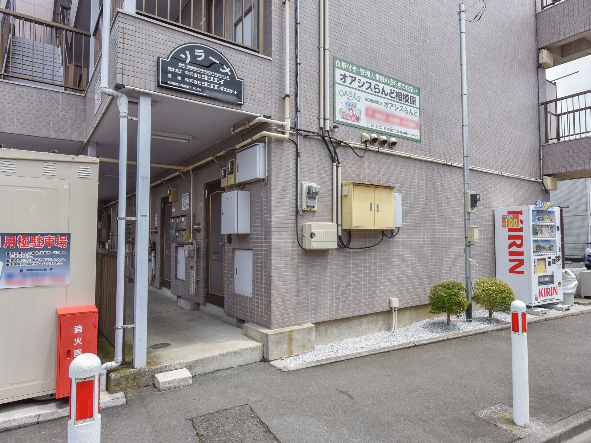 施設はグレーのタイルが貼られた外壁で、壁には施設名が書かれた看板がつけられている。消火器が入れられたボックス、自動販売機も近くにある。
