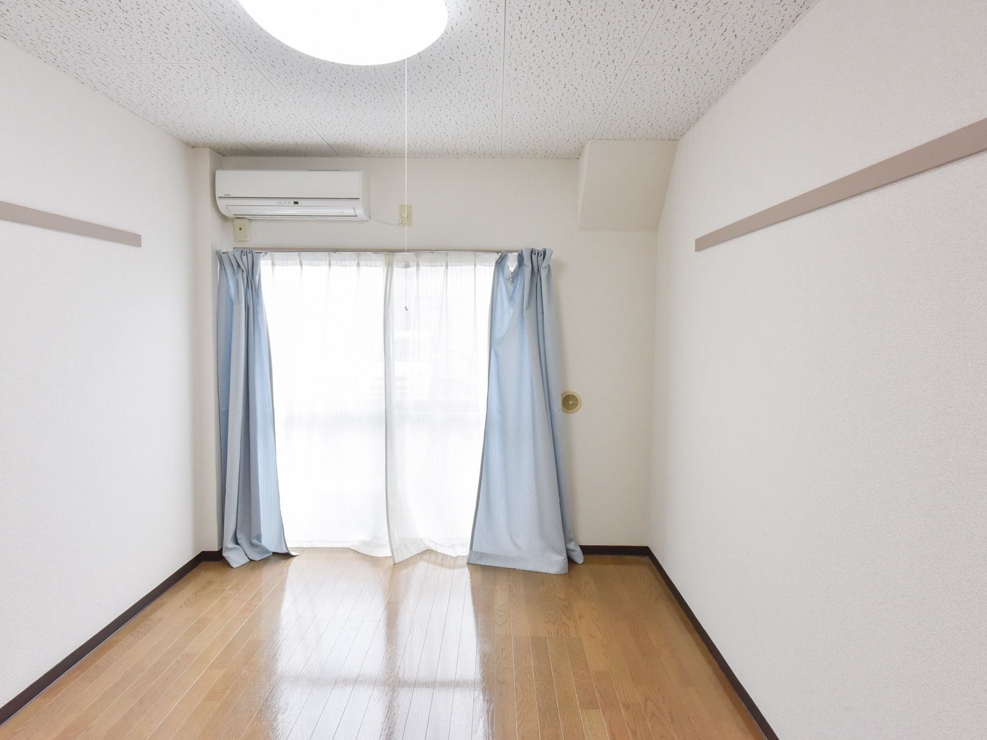 居室の掃出し窓のカーテンレールには、レースと淡い水色のカーテンが掛けられており、爽やかな空間を演出している。
