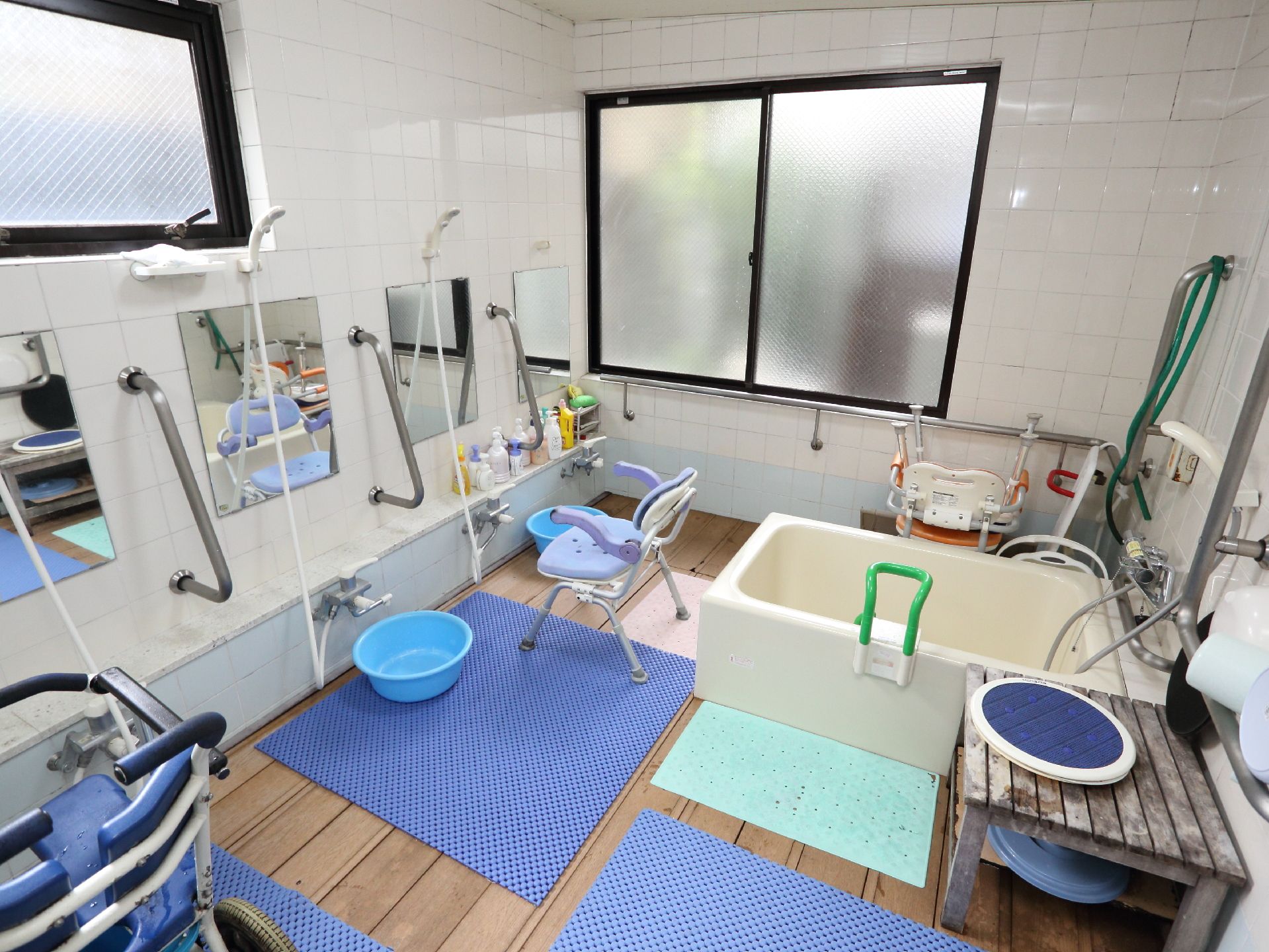 浴室には介護施設でよくある背もたれ、肘掛け付きの耐水性のパイプ椅子の他に車いすタイプの物も置かれている。