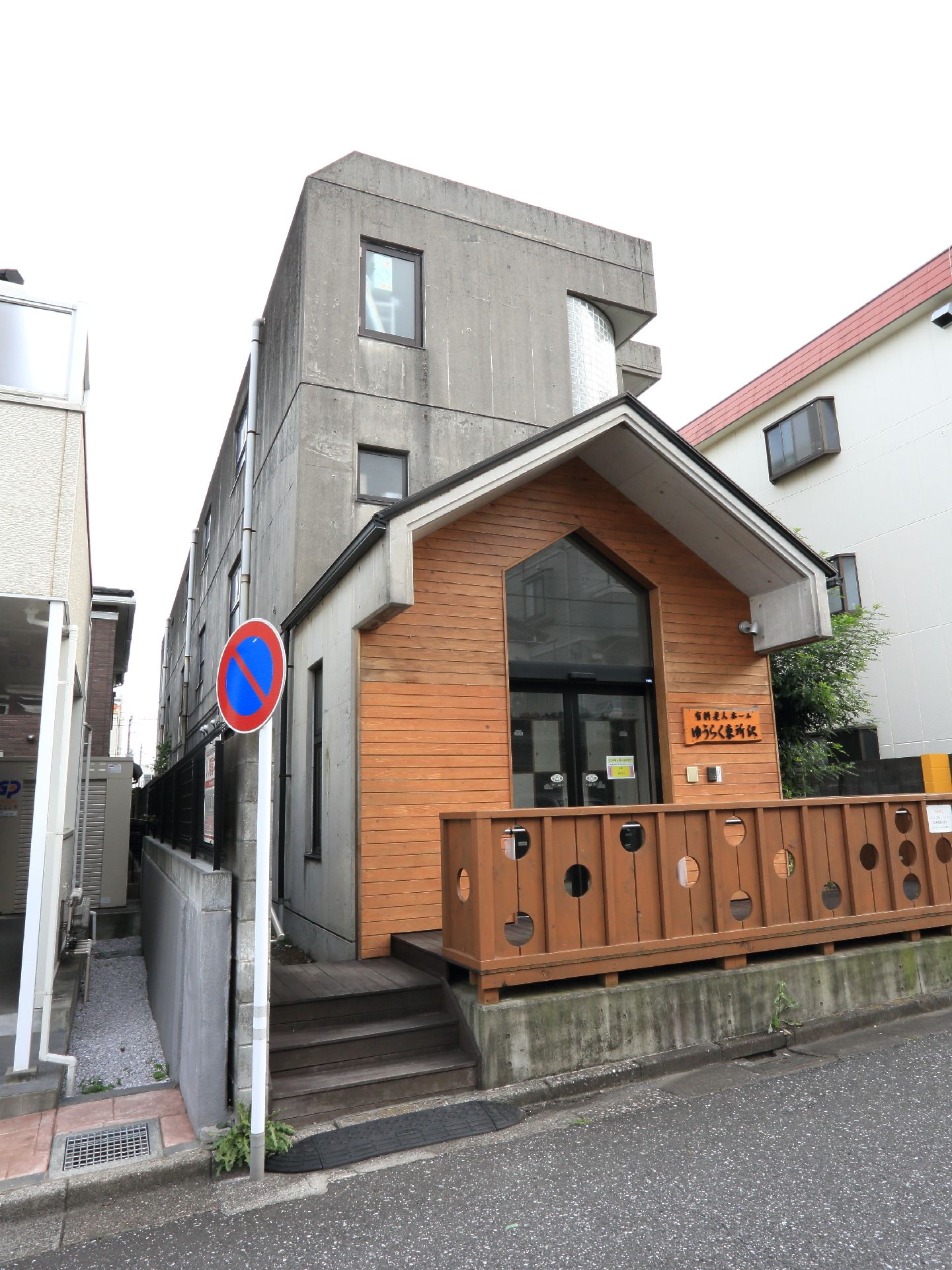 施設は、鉄筋コンクリート造りの3階建て。エントランスには、丸い穴の開いた木製の塀が取り付けられている。壁にも木が張られている。