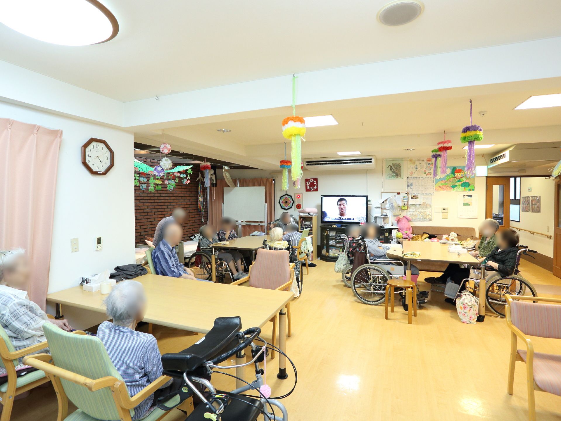 談話室には、大きなテレビがあり、テレビを見ている人がいる。車椅子利用者も快適に使用できるよう、テーブルの高さが高めに作られている。