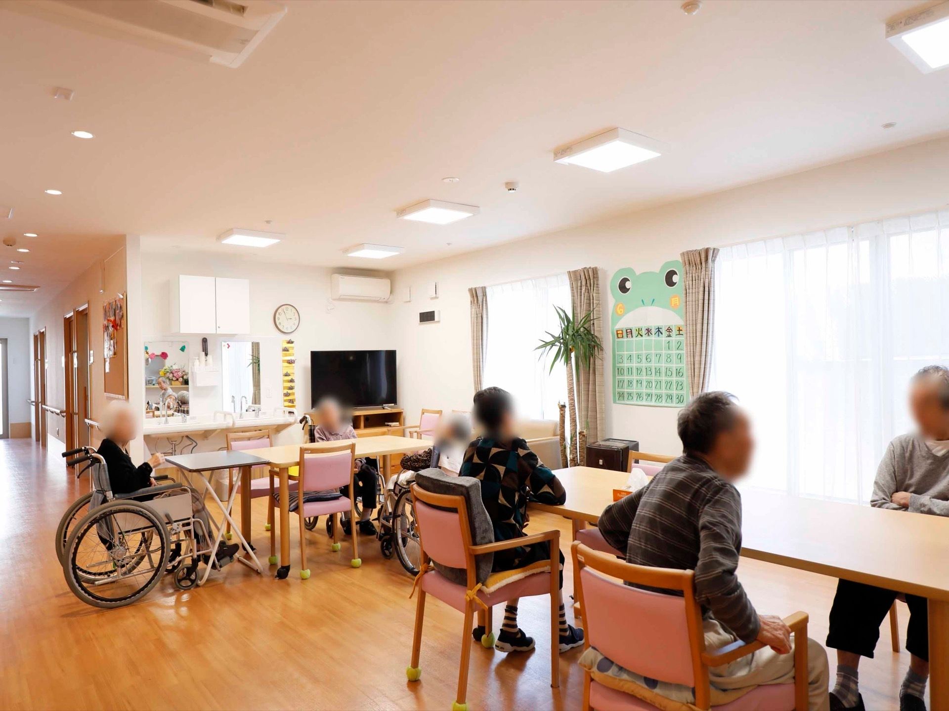 木目調の床、白い壁でコーディネートされた明るい空間である。入居者様が椅子に座り、おしゃべりを楽しむ姿が見られる。