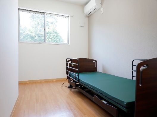 エアコンが付いたフローリングの部屋には介護ベッドがあり、大きな窓も付いている。