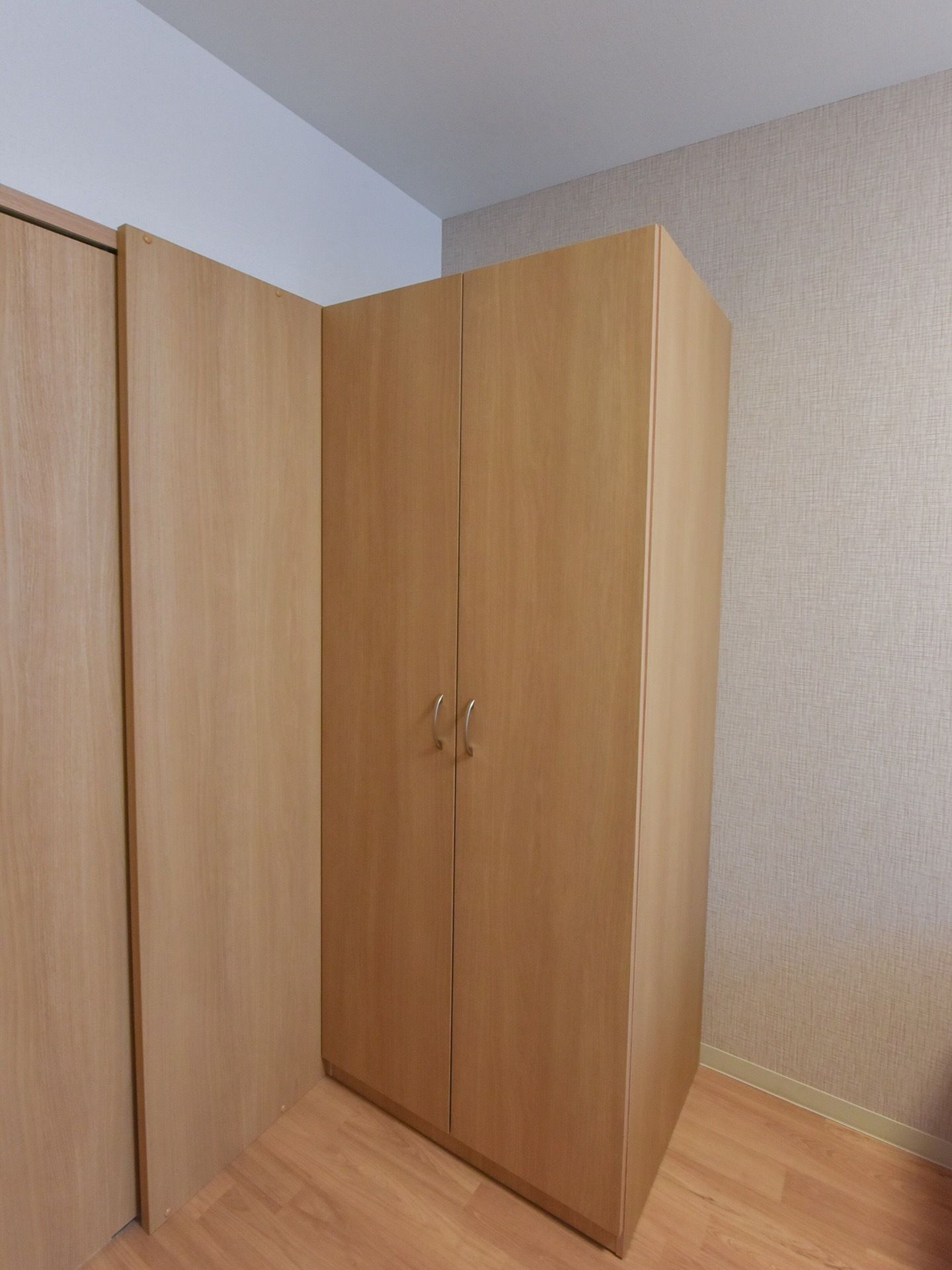 居室内に、高さのある収納用のクローゼットが設置されている。両開きのクローゼットは木の素材であしらわれており、室内の色合いにマッチしている。