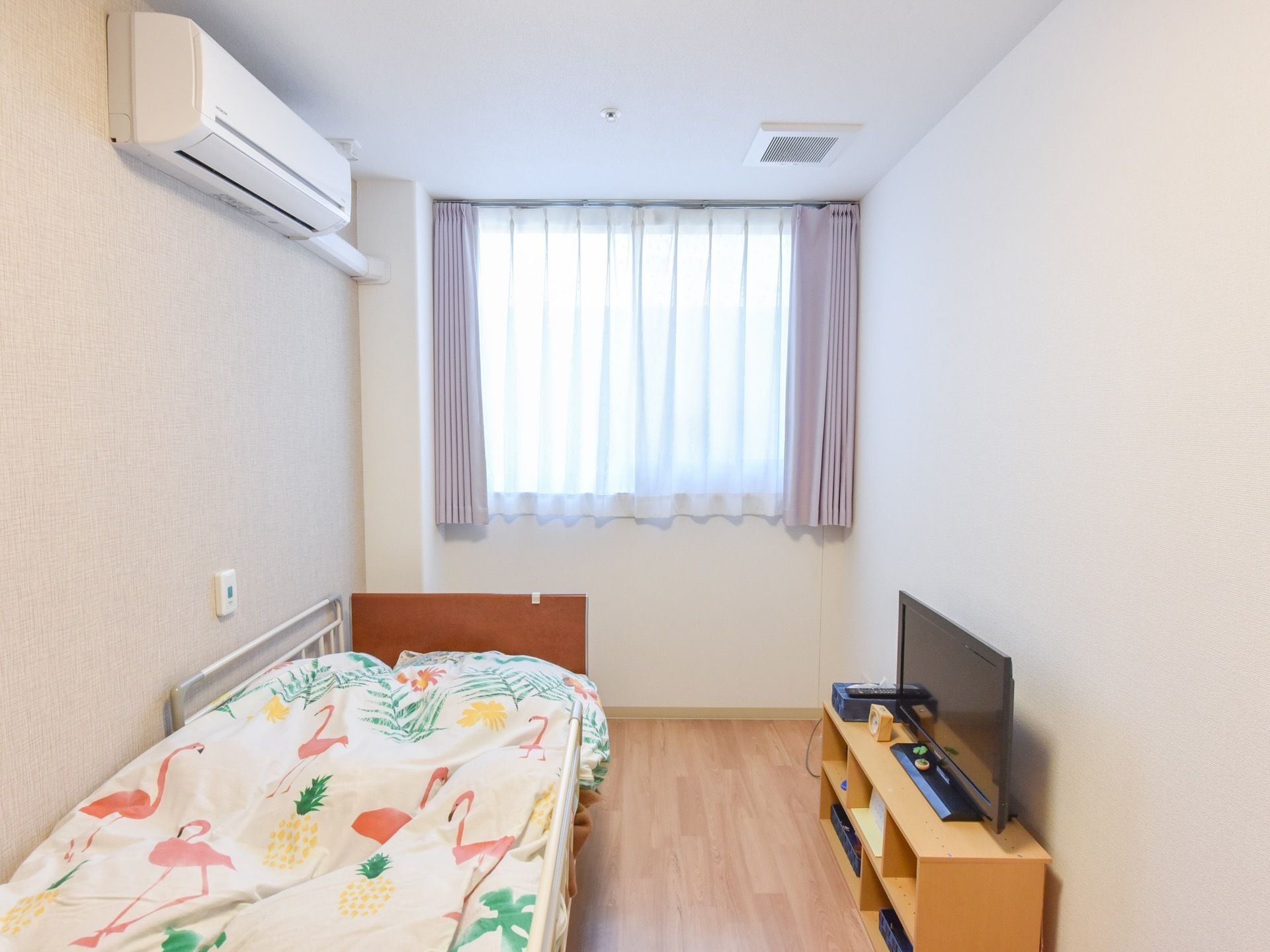 備え付けのベッドには転落防止用の柵が取り付けられている。また、ベッド脇の壁面には、施設スタッフ呼び出し用のボタンが備わっている。