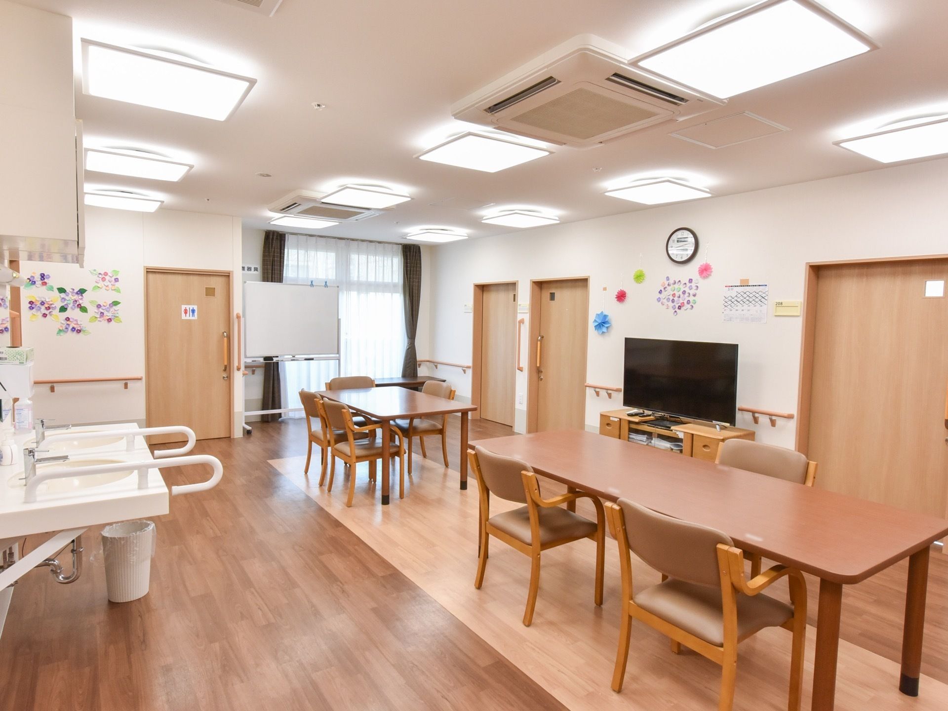 白と木目を基調とした共有スペースは、木のぬくもりが漂う空間である。洗面台とトイレを備え、壁には手作りの花を飾っている。