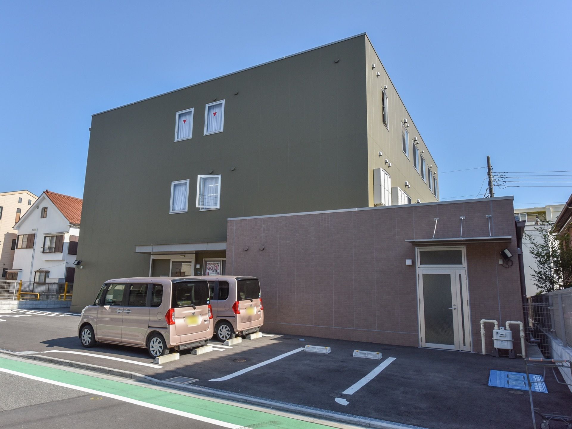 施設は、道路に面したモスグリーンの３階建ての箱型の建物である。住宅街に佇み、敷地内には駐車スペースを設けている。