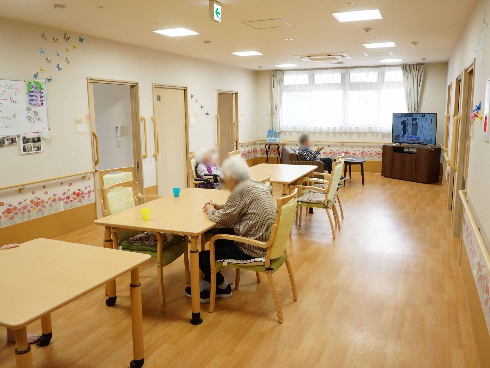 ダイニングテーブルとひじ掛け付きの椅子が複数置かれている。奥の大きな窓にはレースとカーテンが取り付けられている。
