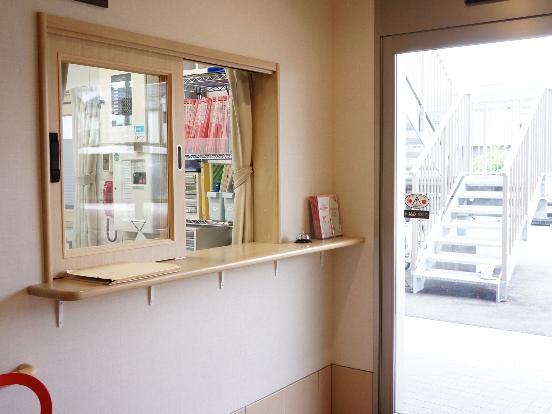 玄関横にガラス窓のついた受付がある。カウンター上には、呼び出し用のベルやパンフレットが置かれている。