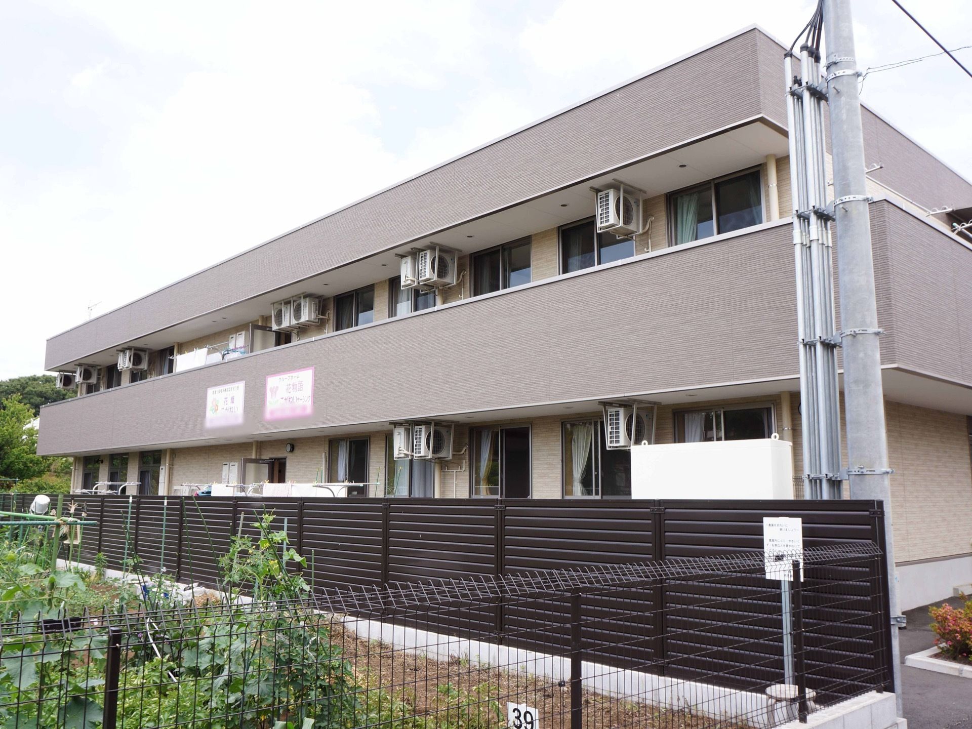 ブラウンを基調とした落ち着いた色合いのグループホームである。施設目の前には、日当たりの良い広い畑が広がっている。