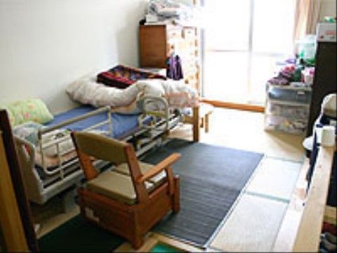 居室は畳敷きで、一部にマットが敷かれている。その上にはベッドが設置されている。ベッドの足元にはタンスがある。