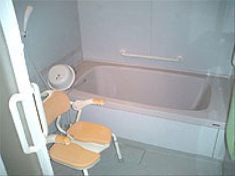 浴室には奥に浴槽があり、隣接している壁に手すりが設置されている。浴槽の手前にはシャワーや入浴用の椅子が見える。
