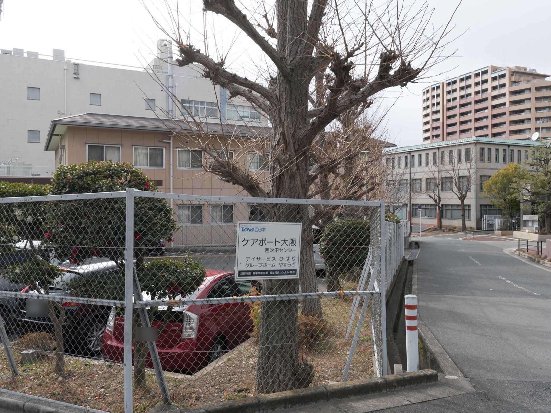 施設は２階建てである。敷地内の駐車スペースには複数の車が停められている。周りはフェンスで囲まれている。