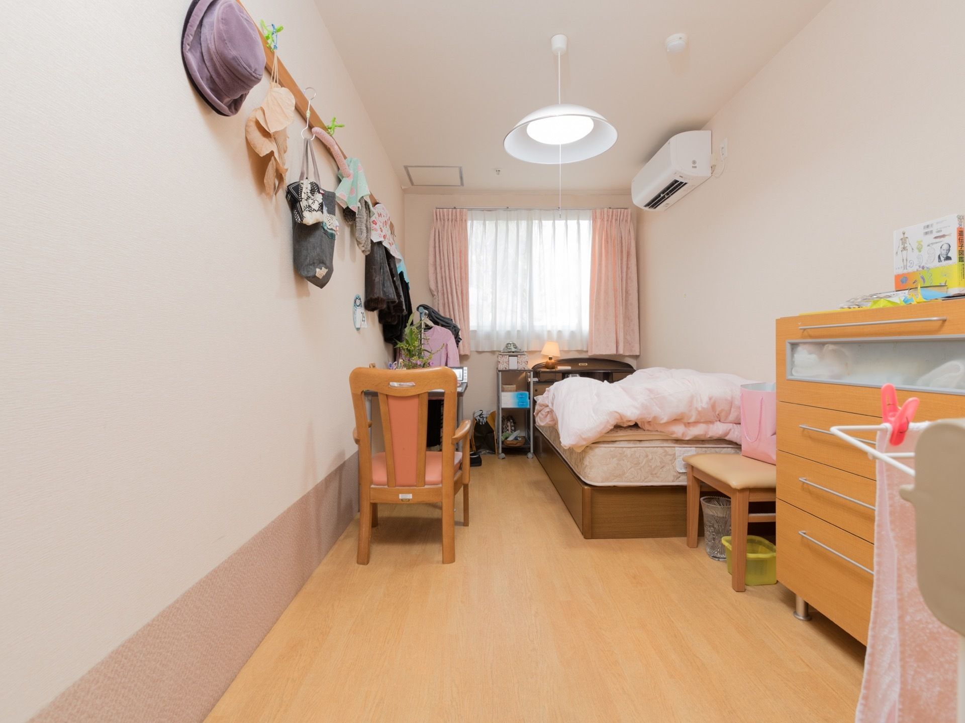 居室にはカーテンがかけられた窓がある。ベッドには布団が置かれている。ハンガーラックや壁掛けハンガーもある。