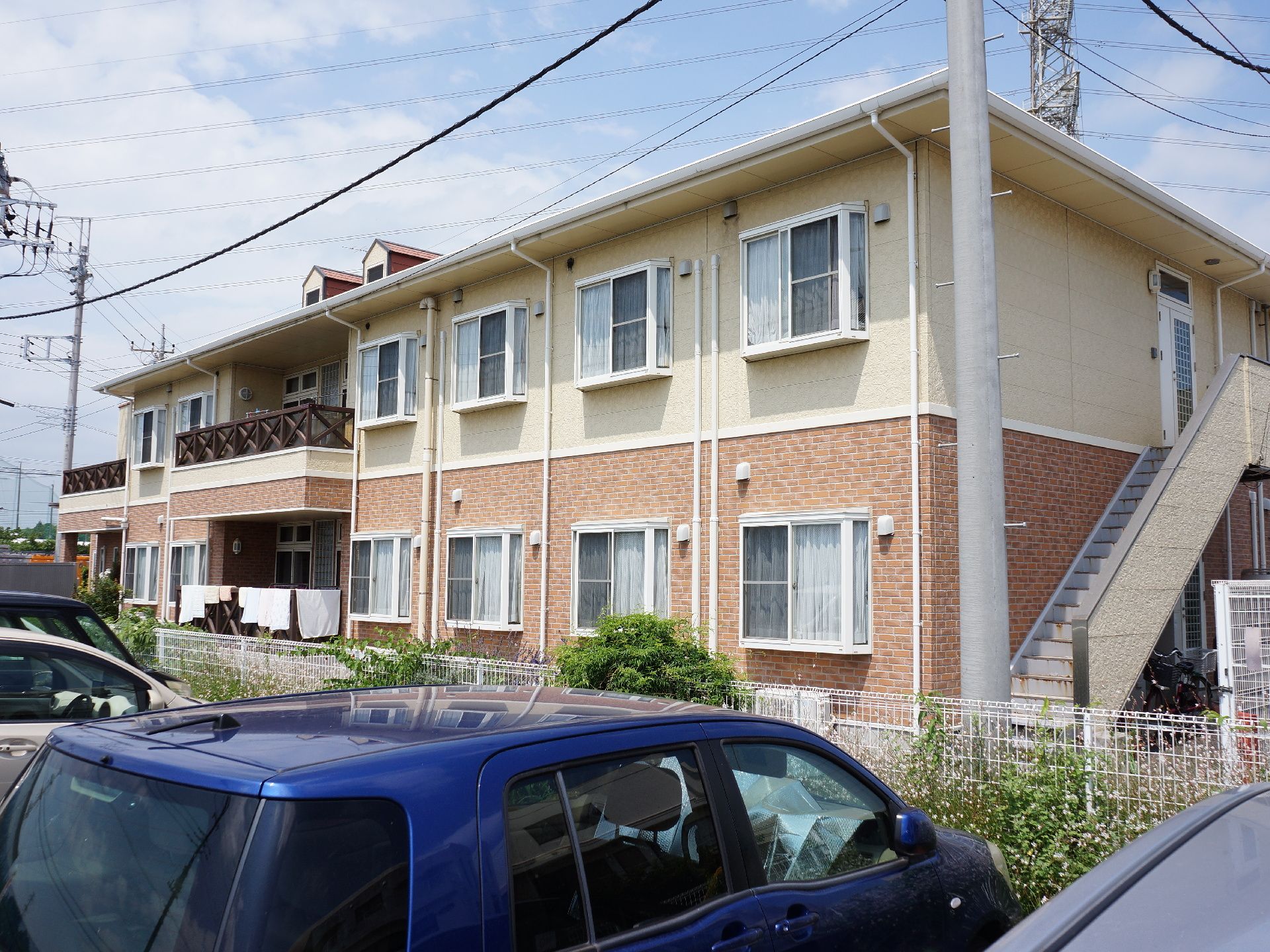 日当たりの良い居室の窓が並んでいる。２階から降りられる非常階段がある。窓は、出窓になっている。共有のベランダ部分に洗濯物が干してある。