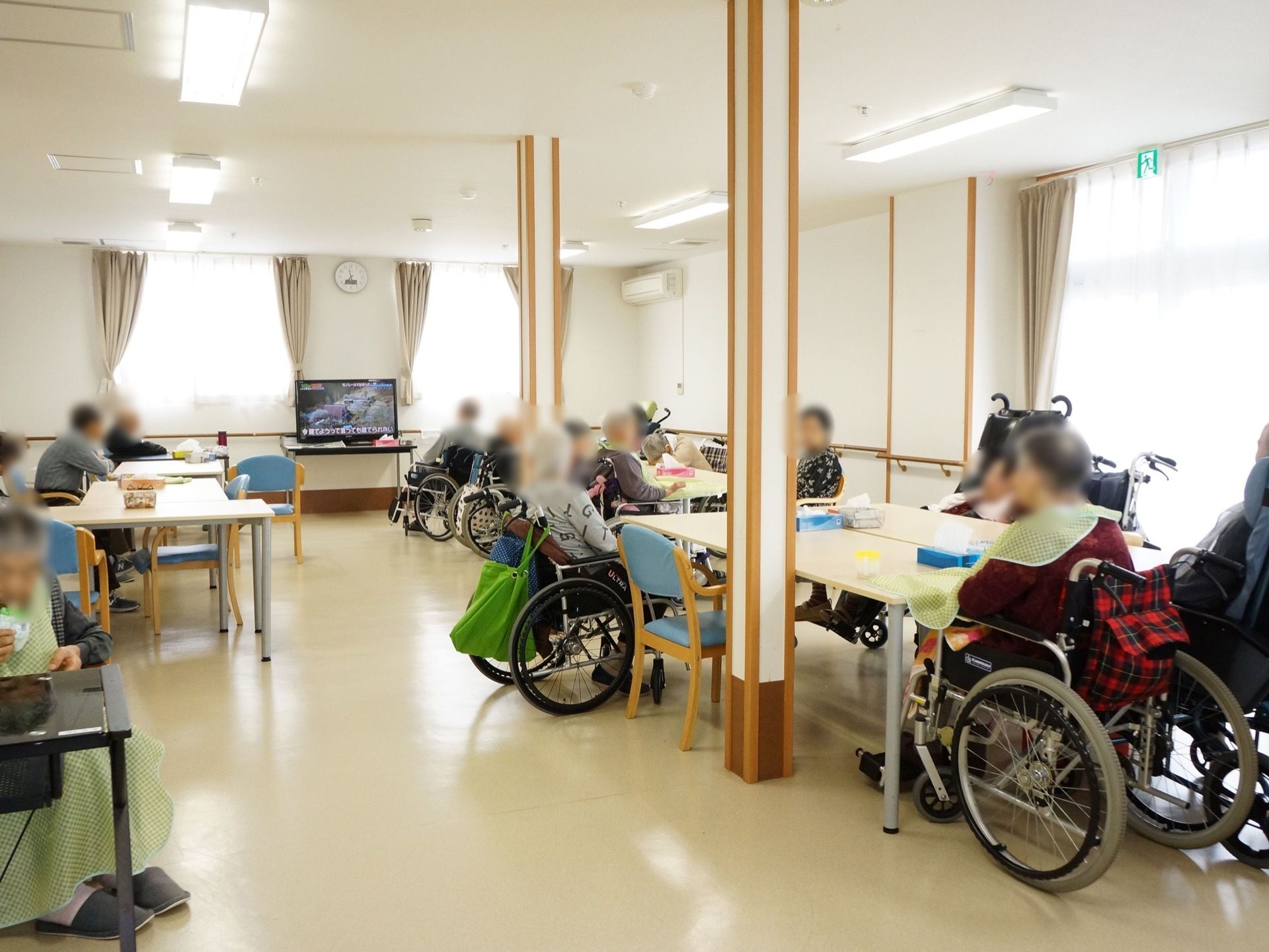 食堂にはたくさんのテーブルが設置されている。車椅子に座ったままで着席している入居者様がいる。窓際には液晶画面のテレビがある。