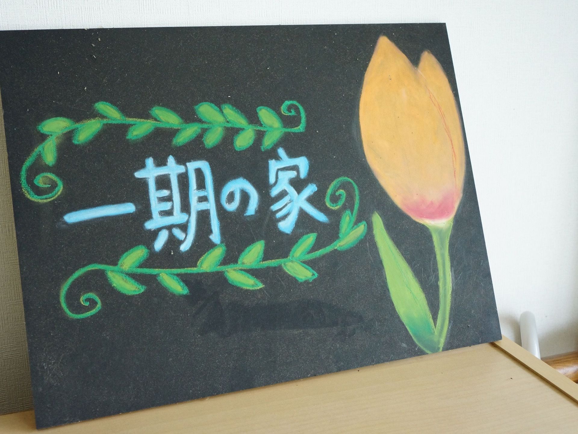黒い小さな黒板にチューリップが描かれ、その横に施設名が記載されている看板