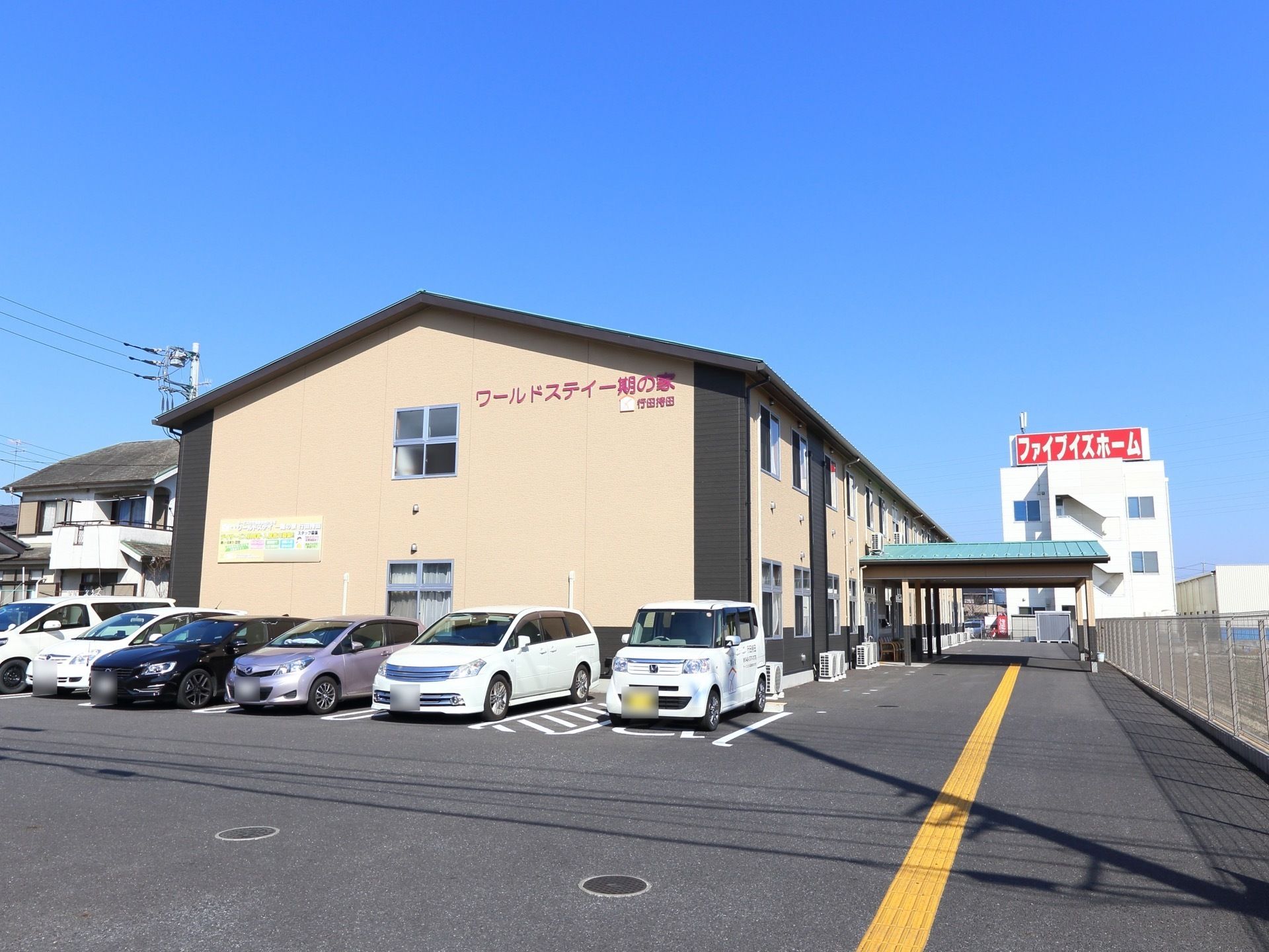 ベージュ系の明るい雰囲気。一般的な集合住宅のような、シンプルな外観である。敷地内には駐車場があり、１番手前は車椅子専用スペースである。