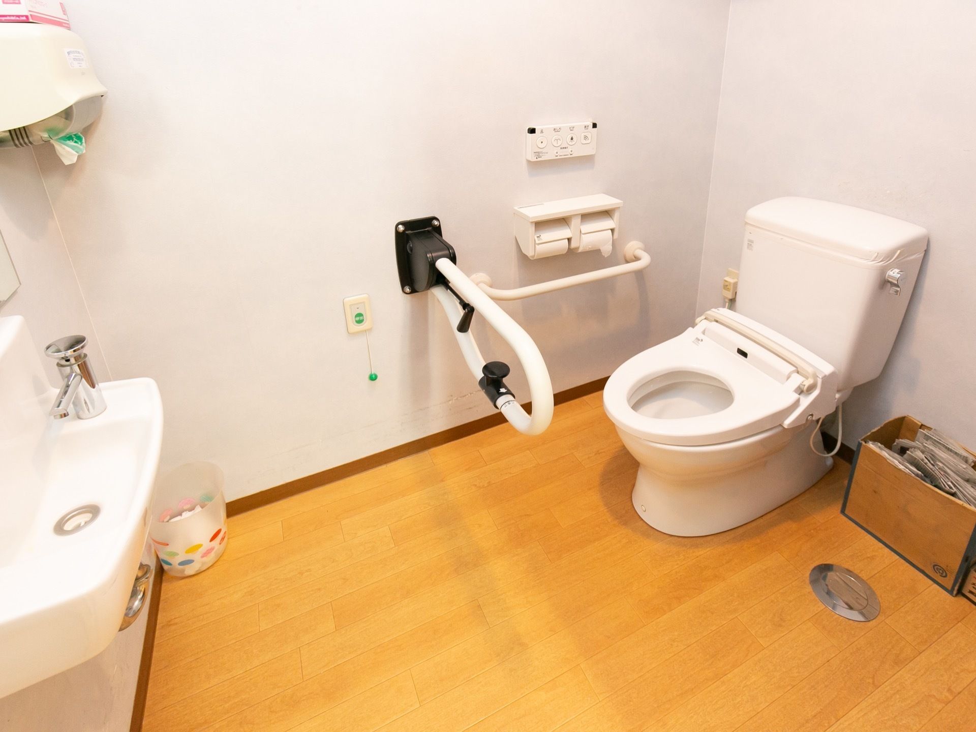 フローリングを採用したトイレで右手の壁際に便座がある。左側には洗面台があり、ペーパータオルがある。