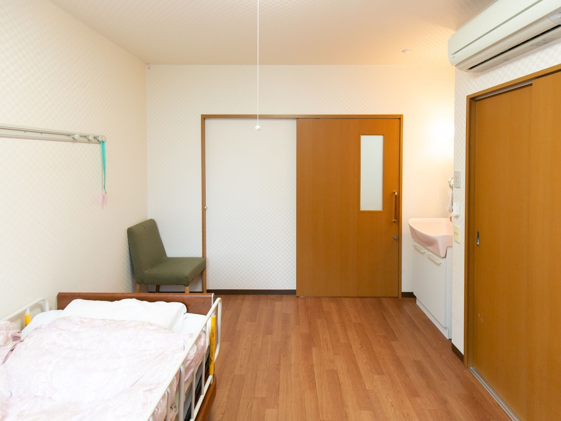居室の入り口は木製扉の引き戸になっている。ドアの前に洗面台があり、照明がつけられている。右手前に押入れがある。