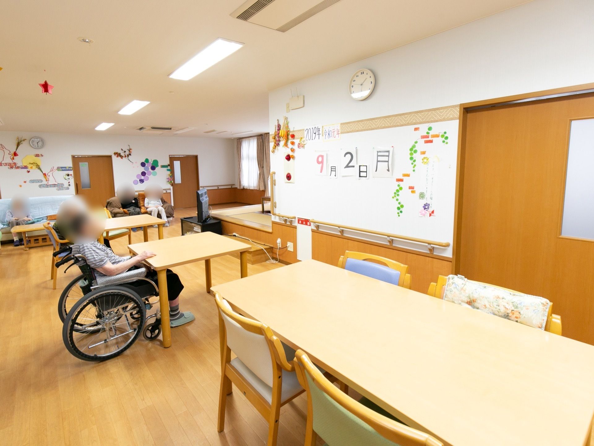 奥に向かって長く伸びている共有スペース。中央にあるテーブルで車椅子をご利用の方が、のんびりとくつろいでいる。