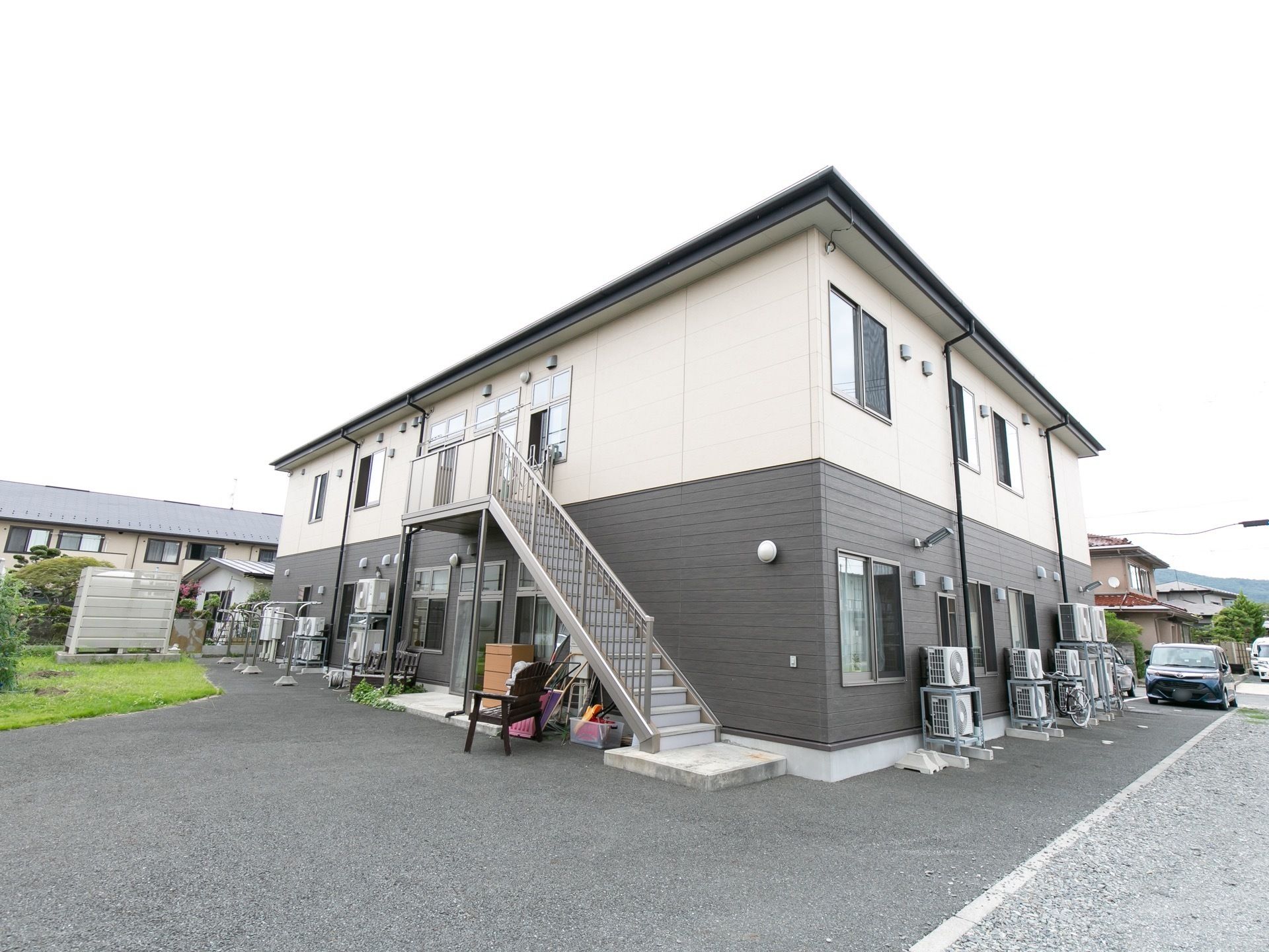 白と黒のツートンに分かれた２階建ての建物で、外階段が付いている。居室の窓が並んでおり、各部屋の室外機が置かれている。