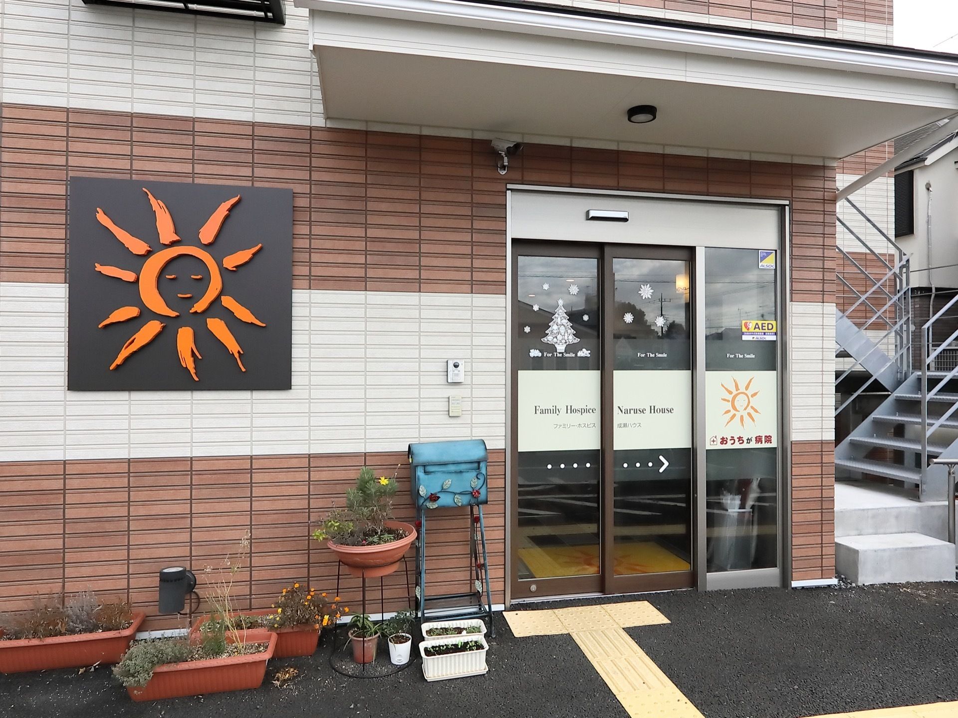 玄関扉はガラスの自動扉になっている。玄関前まで視覚障害者用の展示ブロックが敷かれている。壁にインターホンがある。