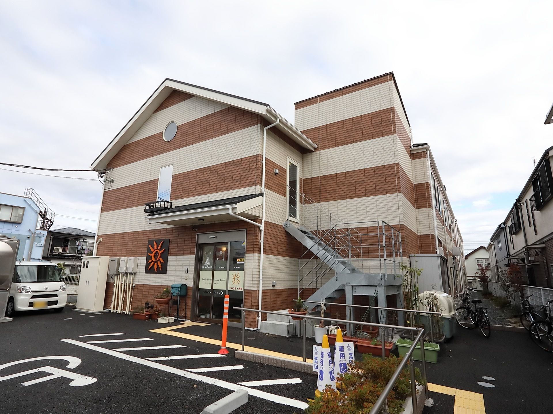 ２階建ての建物は茶色と白で縞模様に塗り分けられている。非常階段が建物に沿って取りつけられ、施設の前は駐車場になっている。