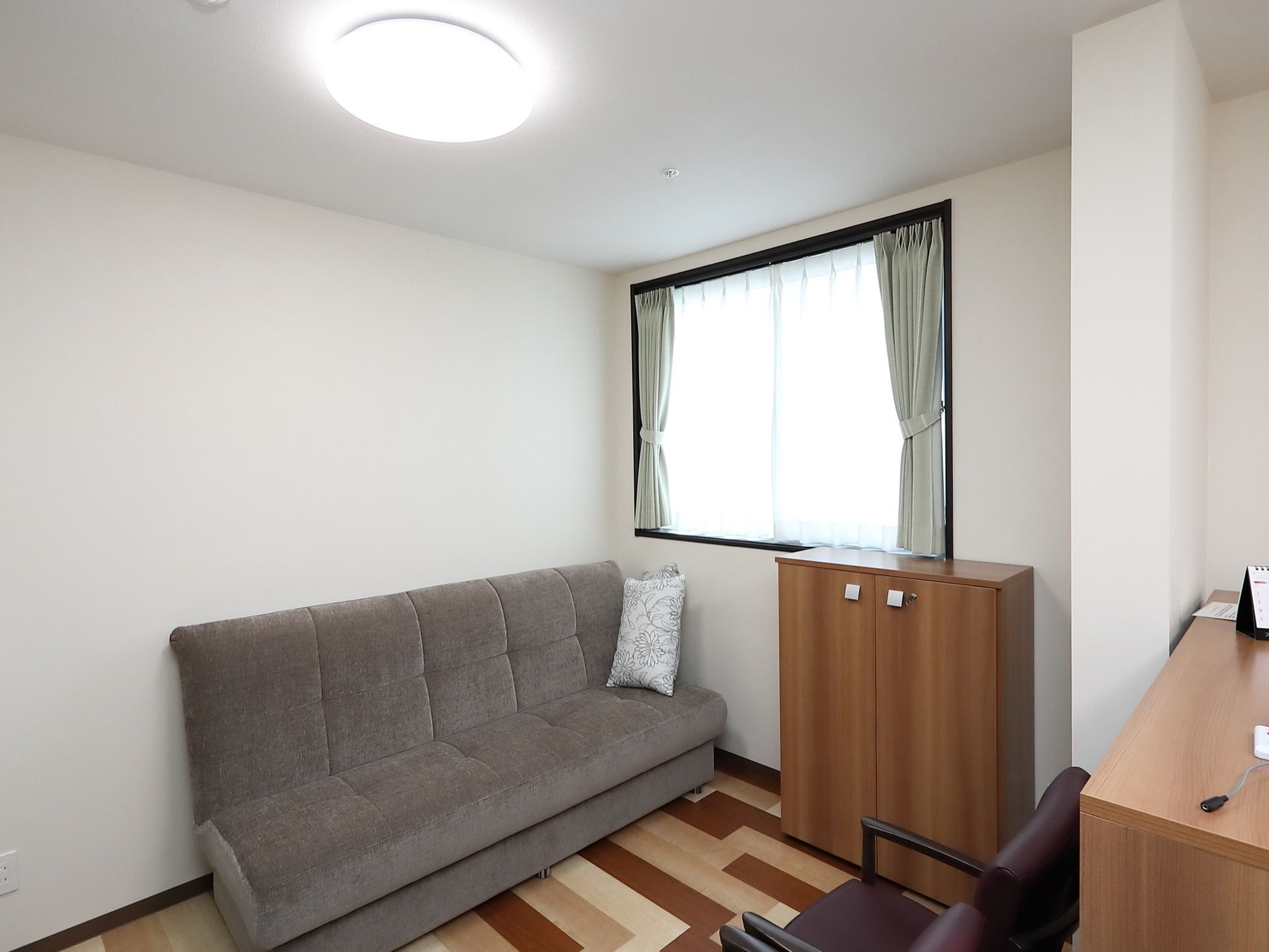 居室には大きな窓があり、その下に観音開きの棚が置かれている。グレーの大きなソファがあり、３人で利用できる。