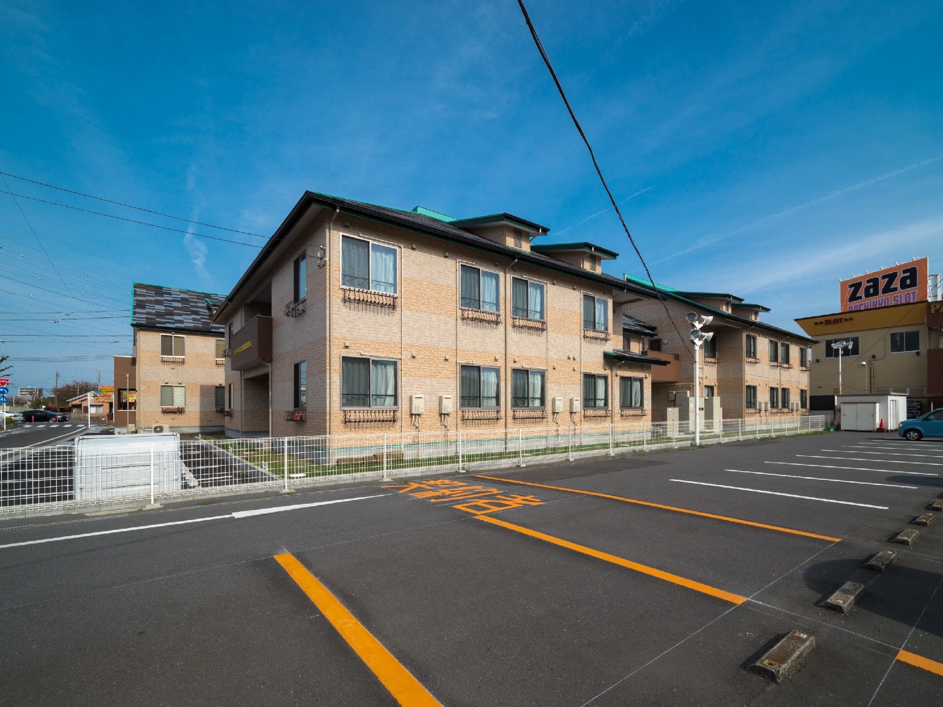 同じつくりの建物が連なっており、それぞれの窓には柵が取り付けられている。建物の入り口前には駐車場がある。