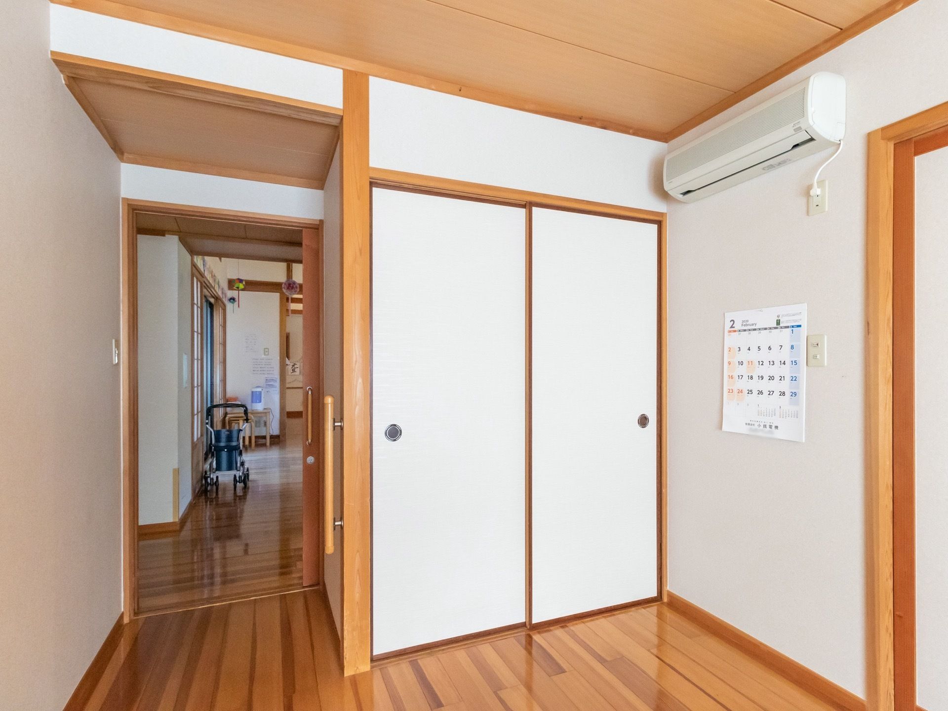 エアコンや押し入れが完備されている居室。部屋の入口はスライド式のドアが採用されており、廊下には車椅子がある。