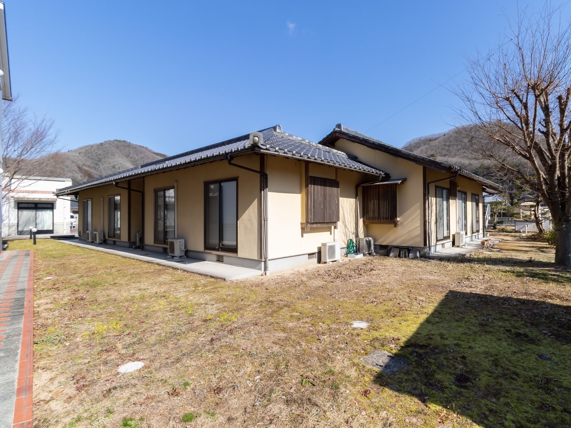 広大な敷地に、瓦葺の平屋建て家屋が数棟並んで建っている。建物の周囲には、雑草の刈られた庭が広がっている。