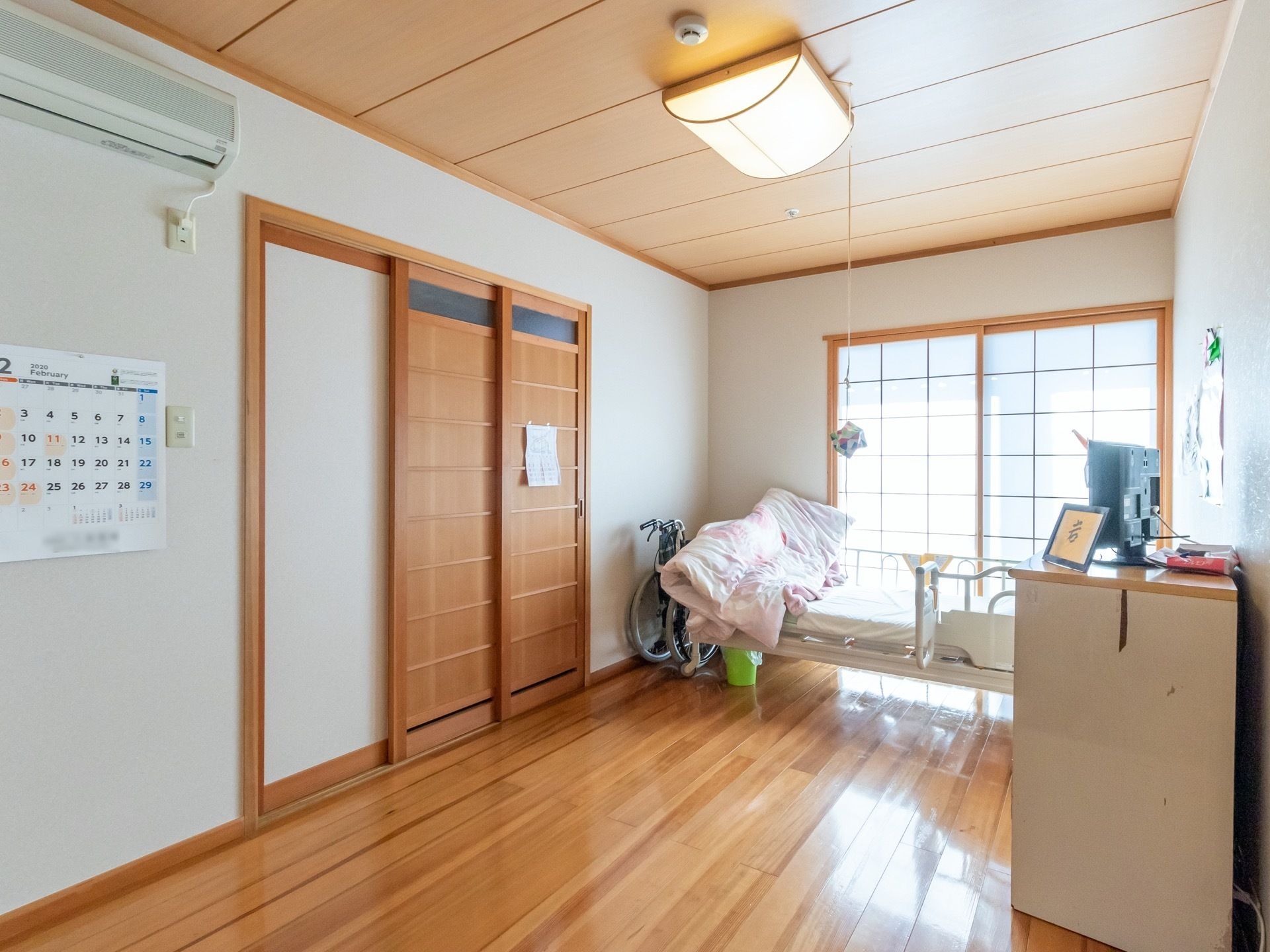 和のぬくもりを感じられる、フローリングタイプの居室。介護ベッドや洋服ダンスが置かれており、壁にはカレンダーが掛けられている。