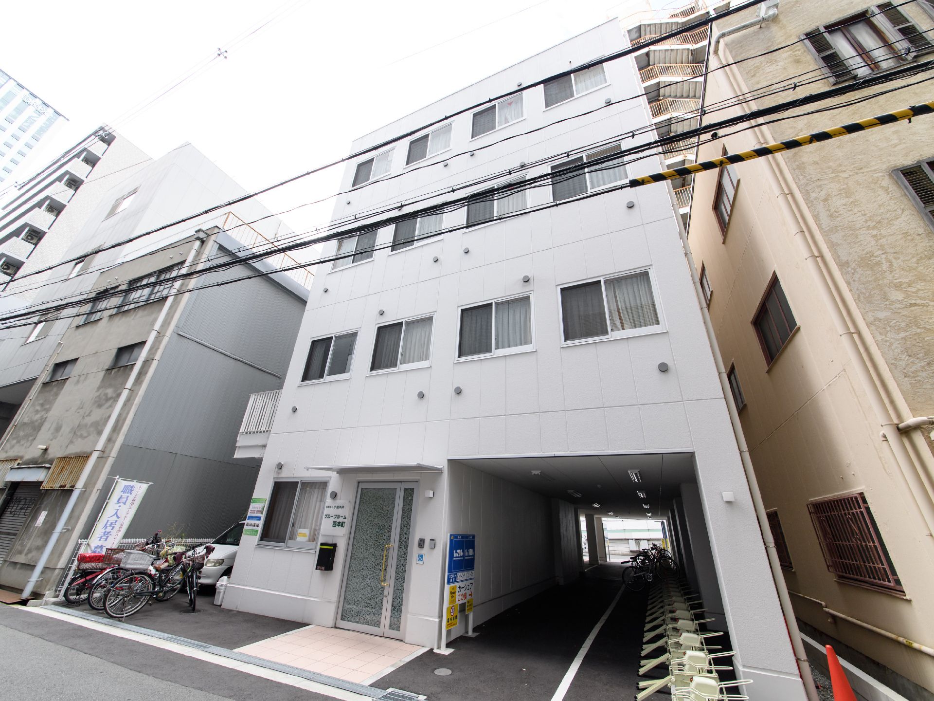 4階建ての施設建物になっている。玄関はバリアフリーの作りになっている。窓と通気口が多く取り付けられている。