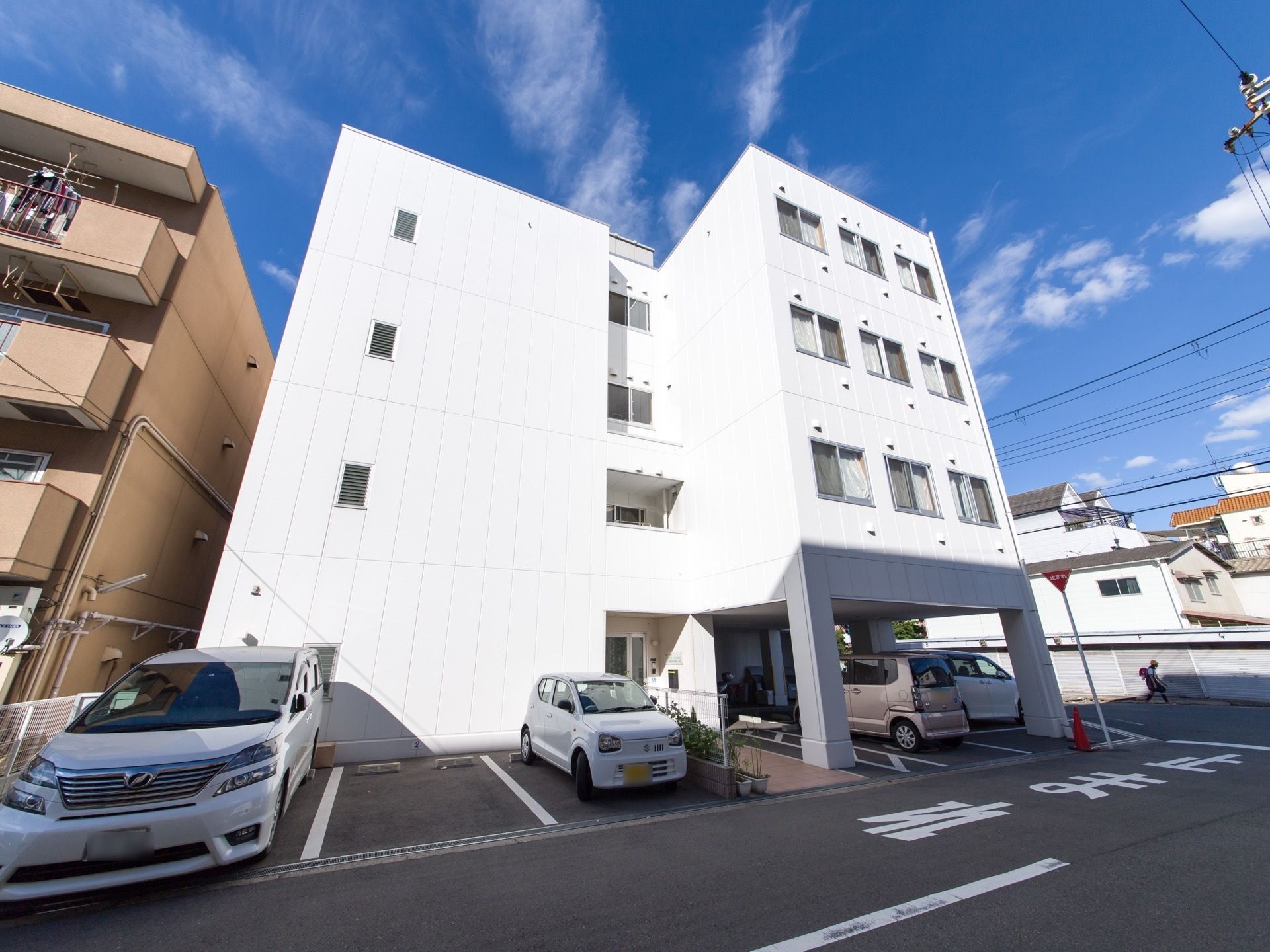 真っ白な4階建ての建物になっている。1階には、玄関や駐車場がある。目の前は道路に面している。駐車場が広い。