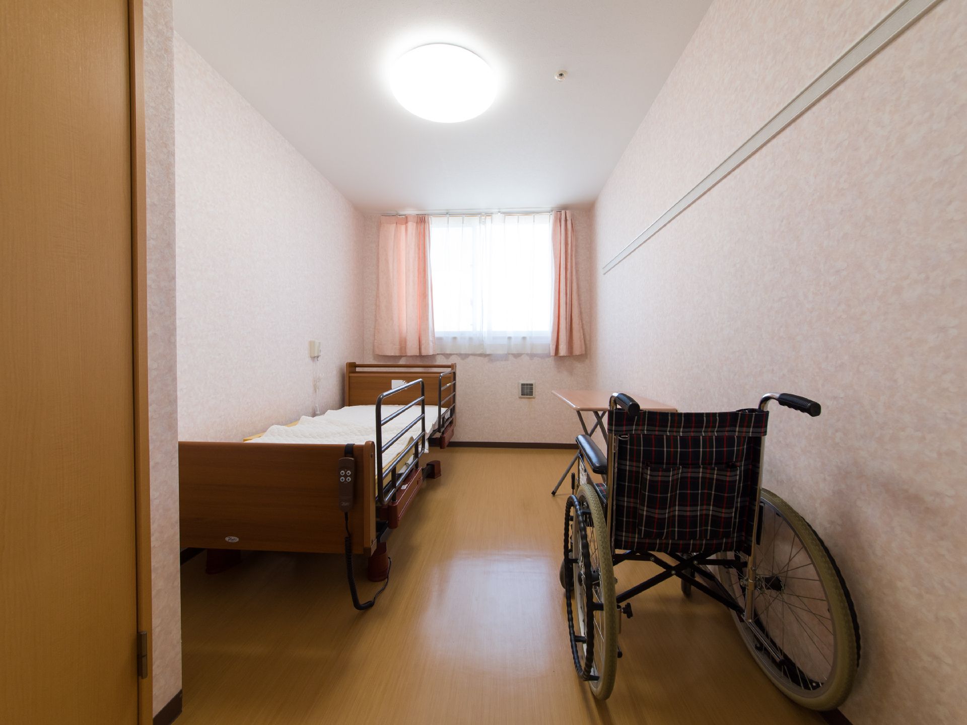 左手に手すり付きのベッドが設置され、右手に車椅子が置かれている居室