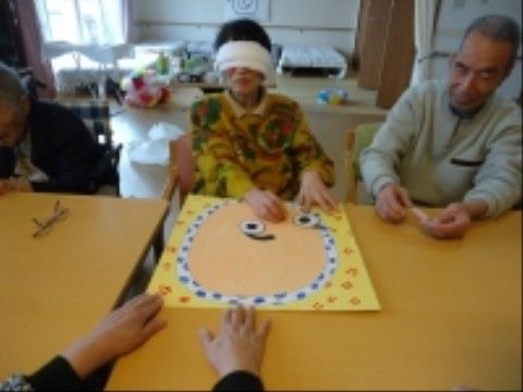 テーブルに着き、目隠しをしてふくわらいを楽しんでいる女性入居者