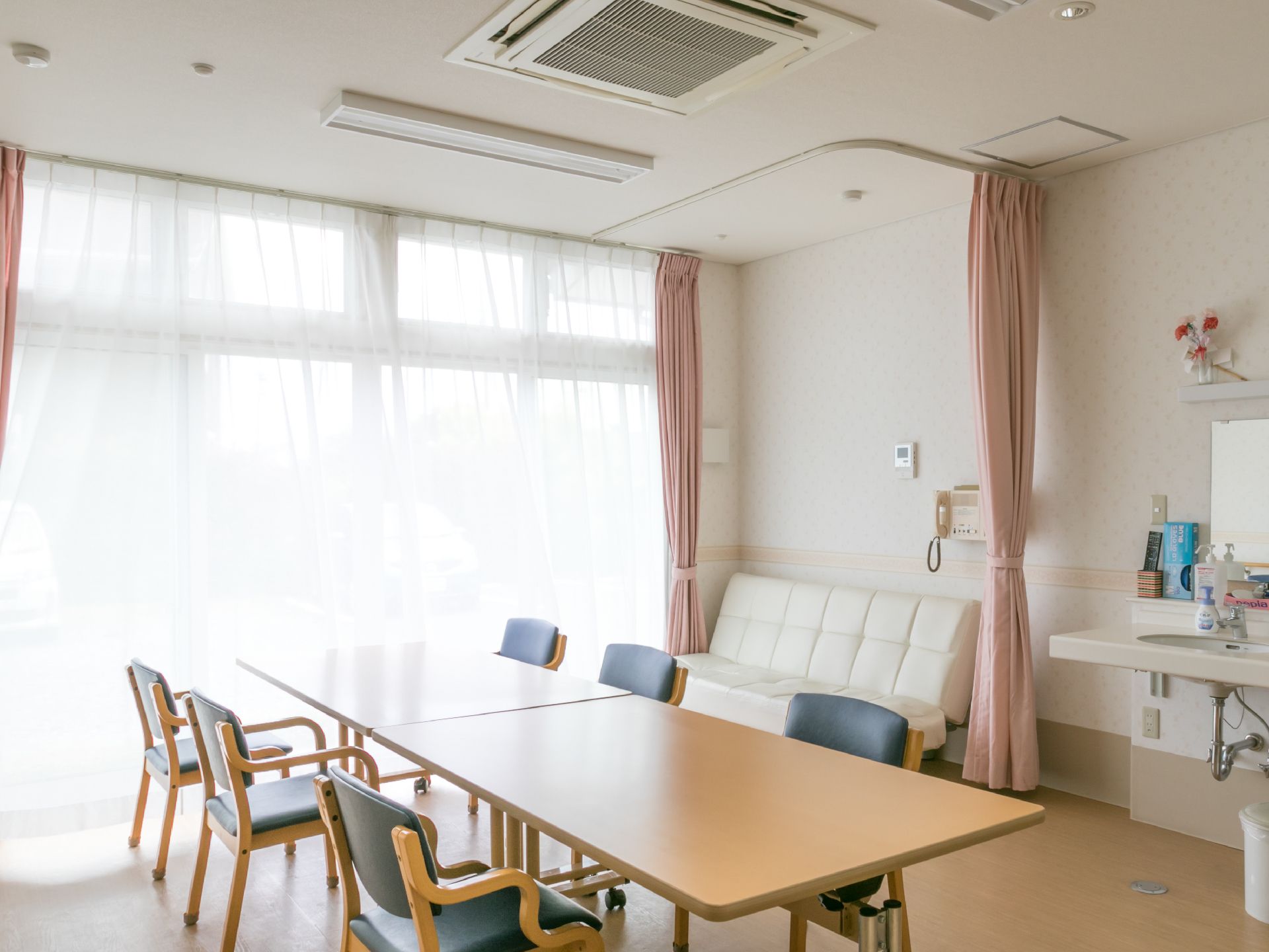 大きい窓から外の光が差し込む明るい室内には、椅子やテーブル、ソファーが並べられている。また、洗面台も設置されている。