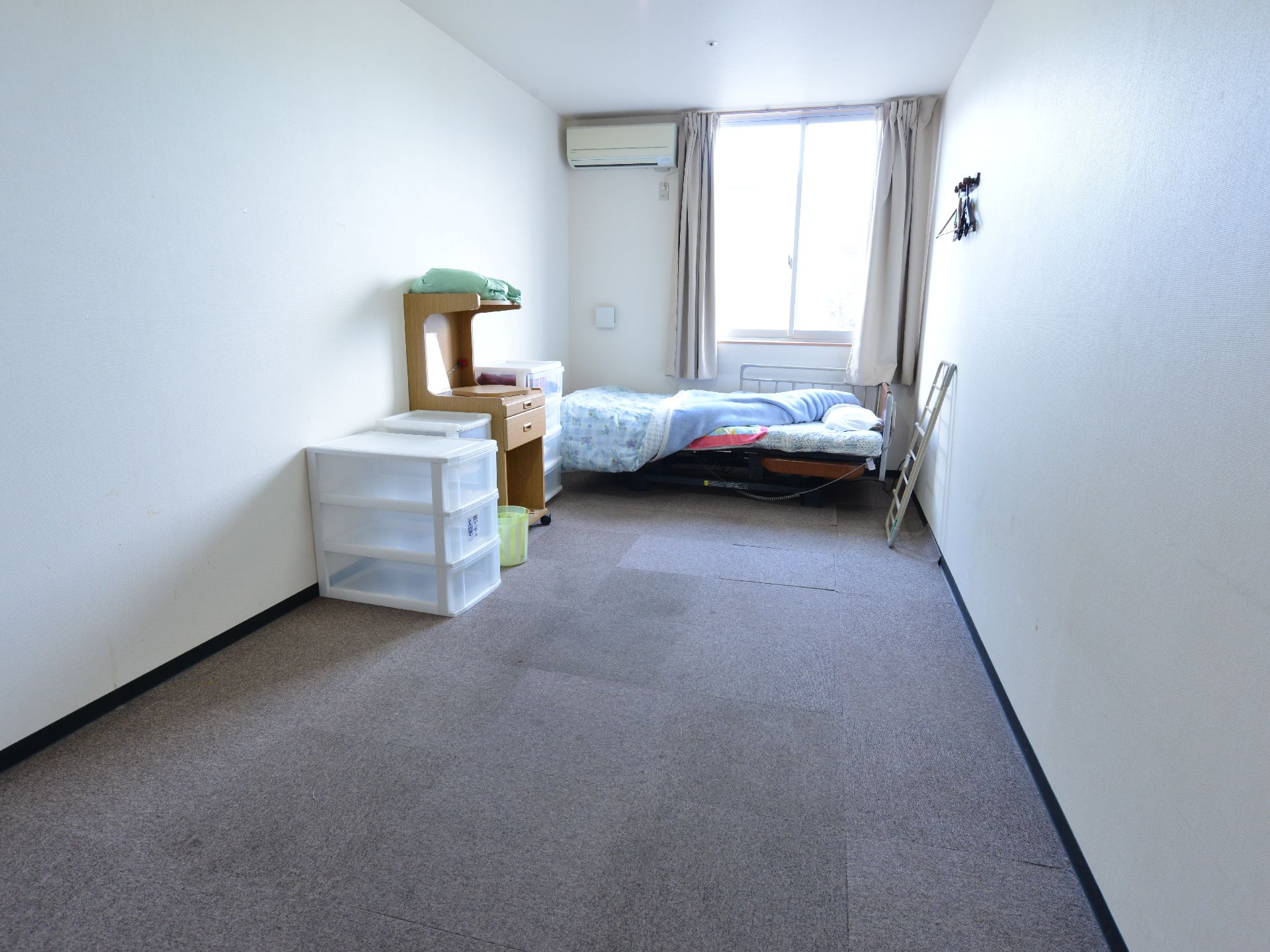 介護用のベッド、エアコン、衣服を収納できるボックス、小物をしまえる引き出しの付いた机が備え付けられている。