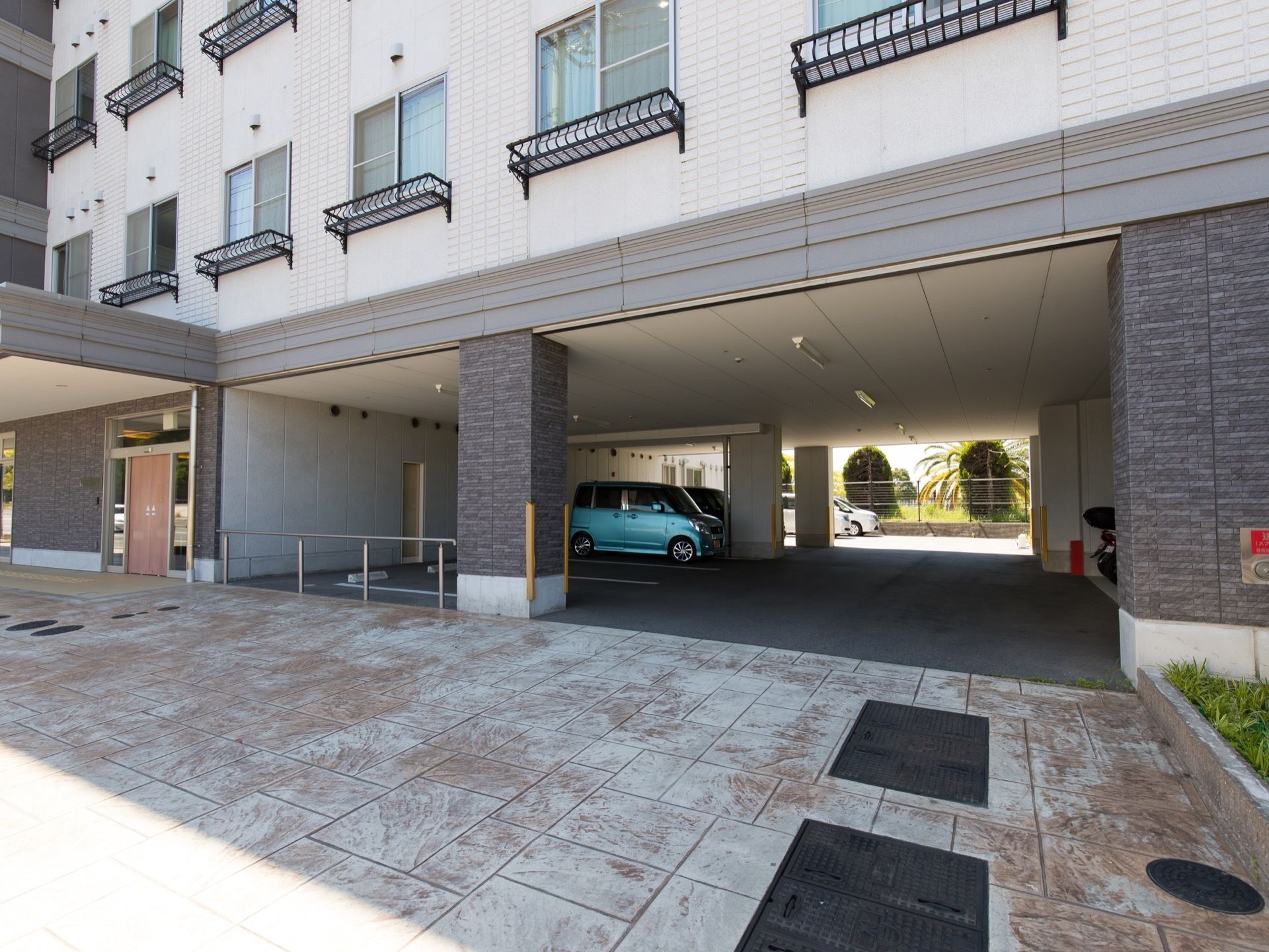 施設の駐車場に車が複数台、停まっている様子である。柱にはクッション材が取りつけられており消火器も置かれている。