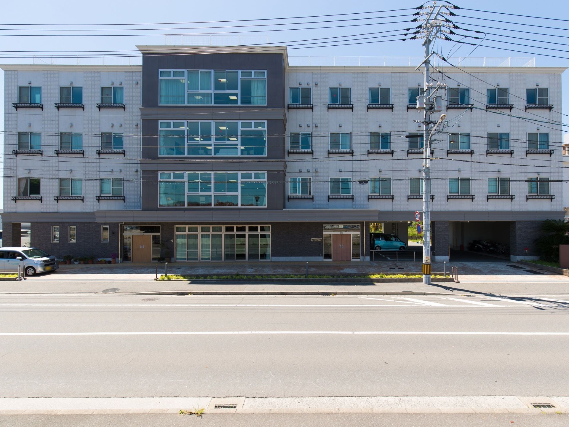 道路に面した、横長の４階建ての建物である。窓が多く並んで配置されており、建物の１階は玄関と駐車場になっている。